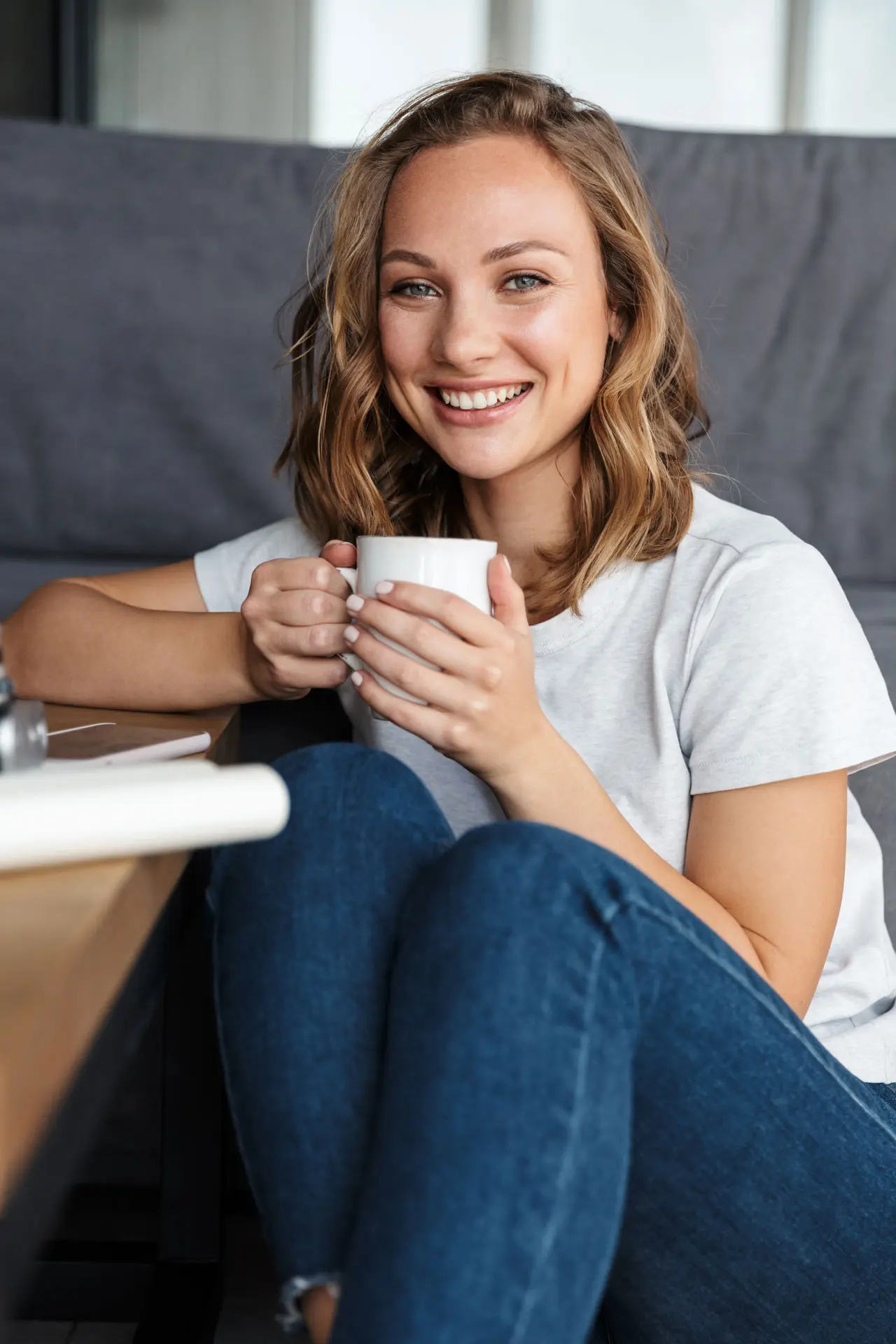 Lächelnde Frau trinkt gemütlich eine Tasse Kaffee zu Hause, möglicherweise nach einer Wurzelbehandlung.