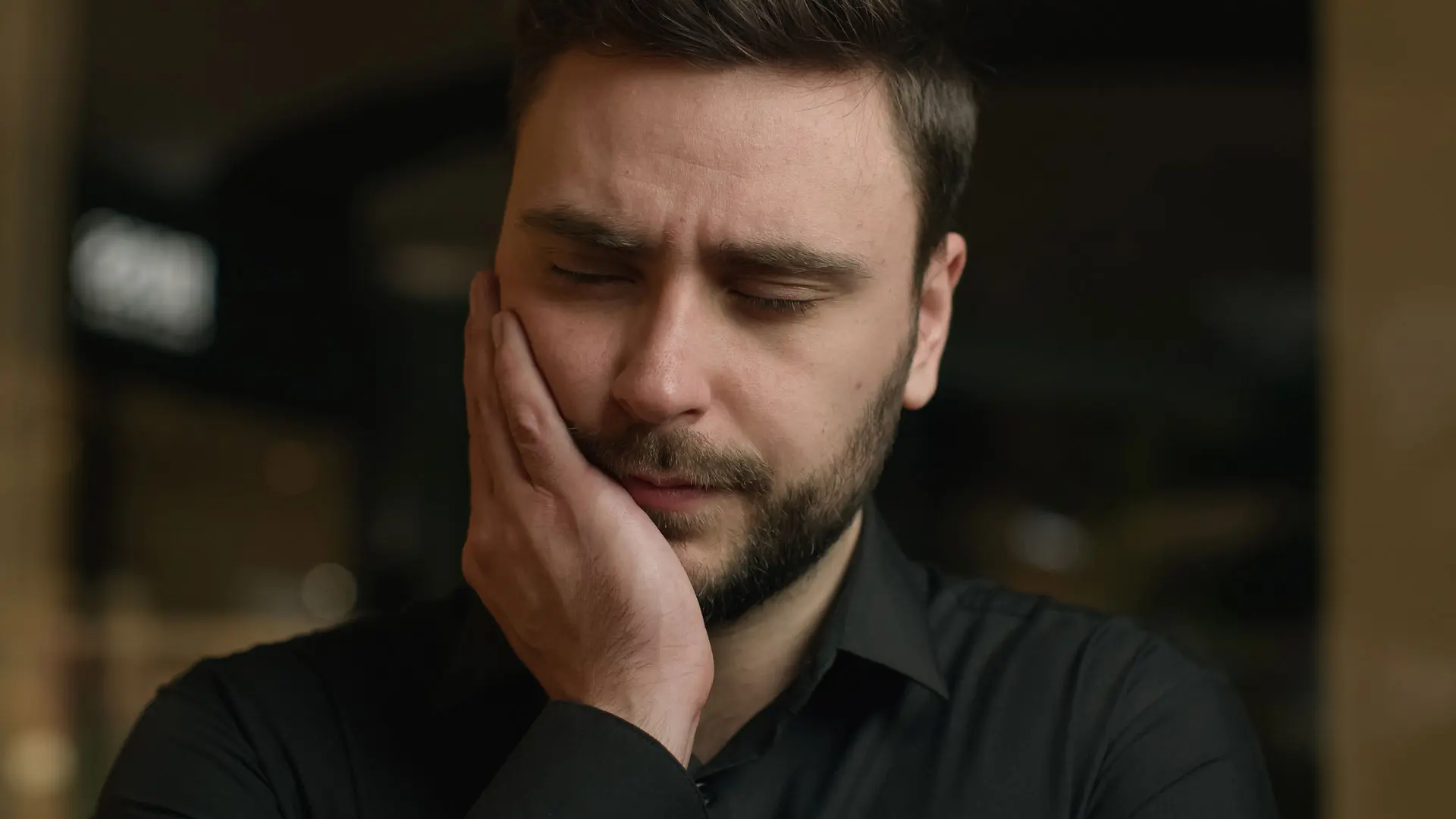 Mann hält sich mit schmerzverzerrtem Gesicht die Wange und leidet unter Zahnschmerzen