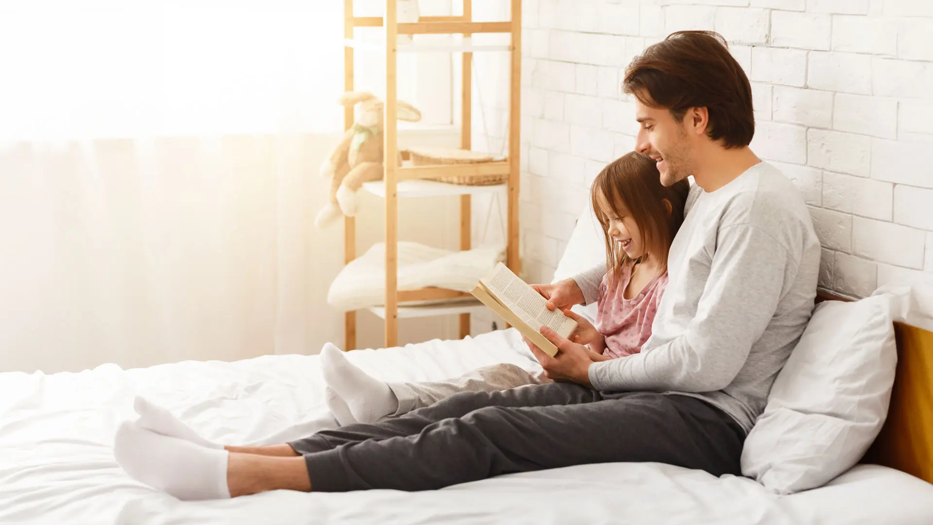 Vater liest seiner Tochter im Bett vor, während beide lächeln und entspannen, nachdem Zahnschmerzen überwunden wurden