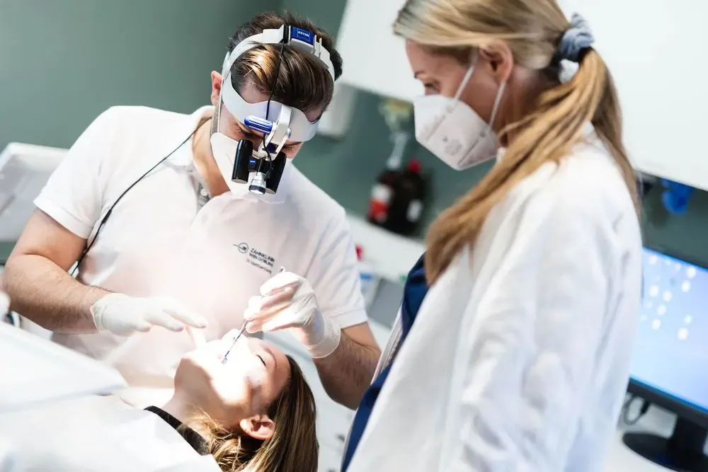 Zahnarzt mit Lupenbrille führt eine Wurzelspitzenresektion bei einer Patientin durch