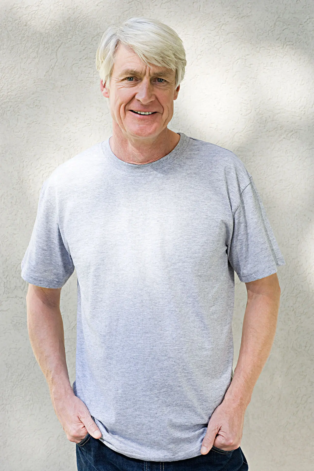 Ein Mann mittleren Alters steht lächelnd vor einer Wand, möglicherweise nach einem erfolgreichen Sinuslift und Knochenaufbau.